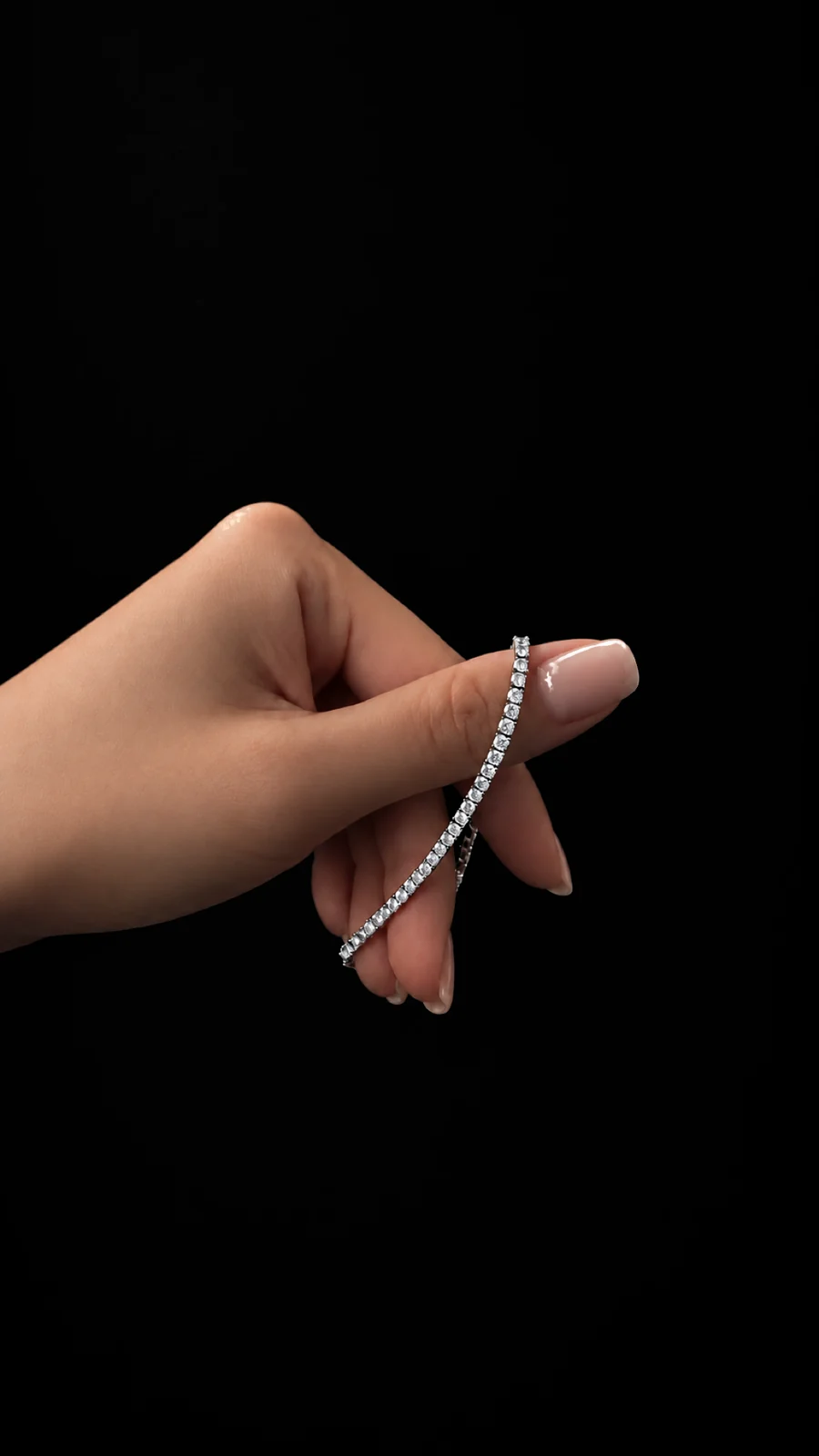 Diamond tennis bracelet draped over a hand against a black background